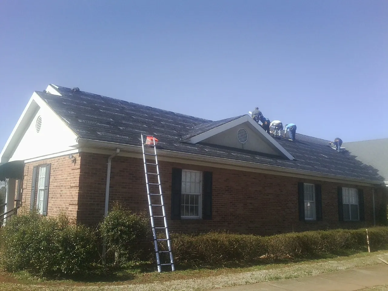 Crew tearing shingles off a brick ranch roof with a ladder set — Metal Roof Repair work by our crew in Barryville