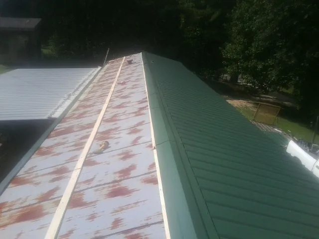 Old rusted panels beside newly installed green metal roofing in Barryville