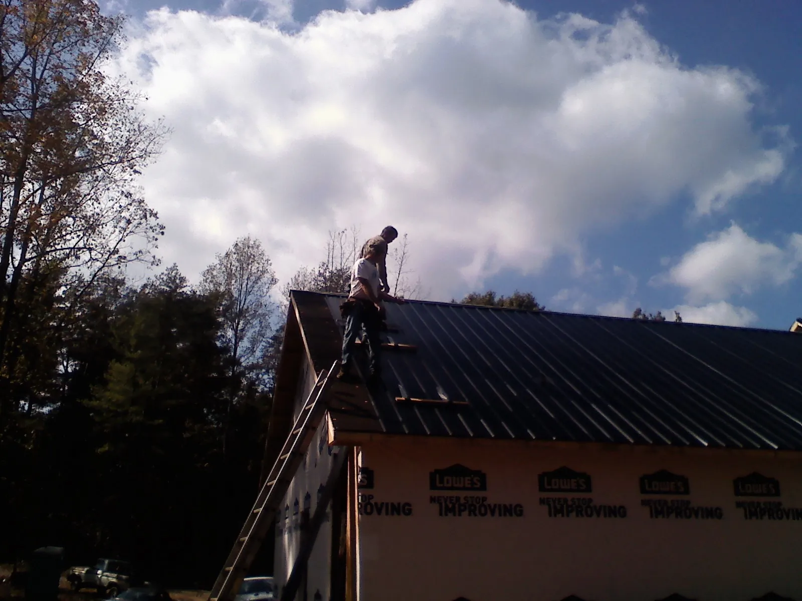 Roofer fastening dark metal panels high against a cloudy sky, from a Roof Inspection job in Barryville