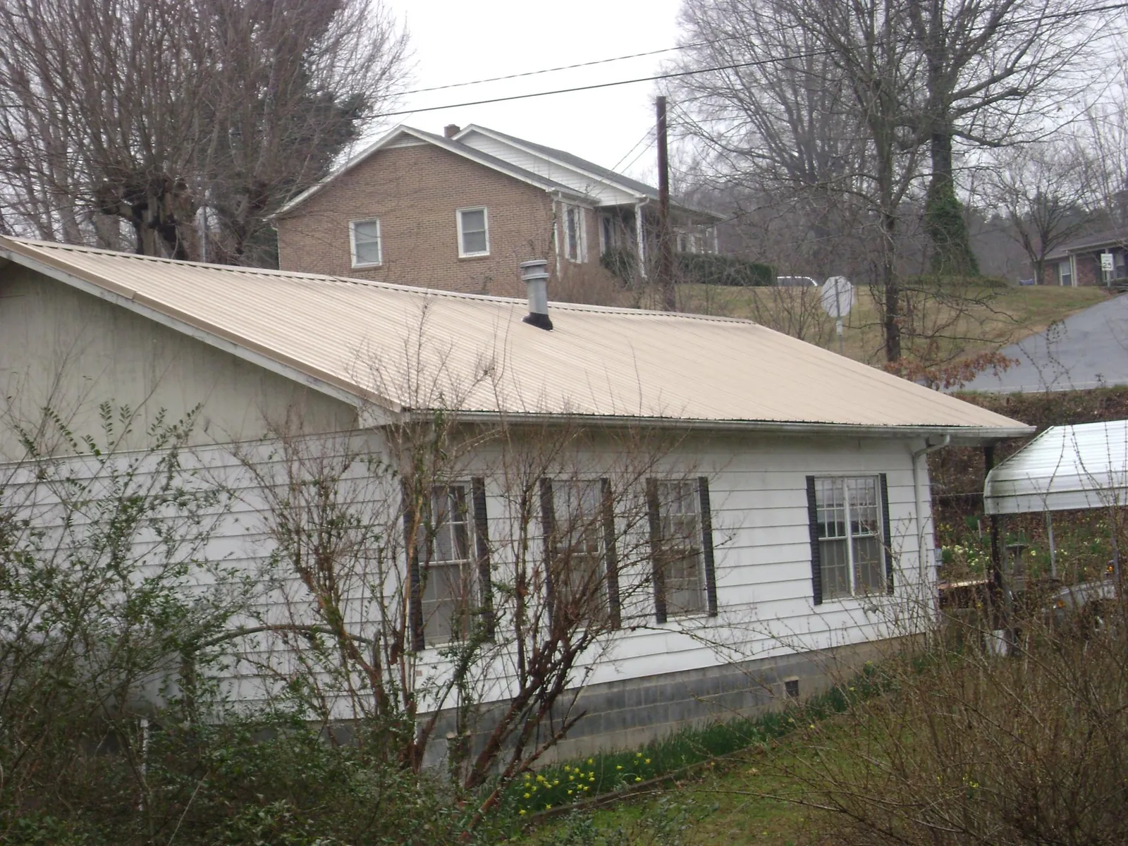 Tan metal roof on a white sided house set into a hillside — Commercial Roofing by Roofing Brothers in Barryville